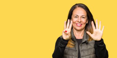 Güzel orta yaş kadın giyiyor kış yelek gösterme ve parmakları ile işaret kendinden emin ve mutlu gülümseyerek süre sekiz numara.