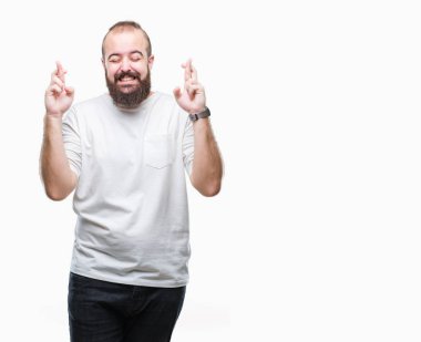 Geçiş parmakları umut ve gözler gülümseyen izole arka plan üzerinde rahat t-shirt giyen genç beyaz hipster adam kapalı. Şans ve batıl kavramı.