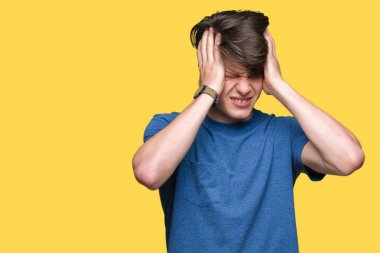 Genç yakışıklı adam mavi tişört giyiyor çünkü umutsuz ve stresli baş ağrısı acı izole arka plan üzerinde ağrı ve migren. Ellerini kafasına.