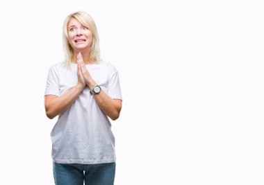 Yalvarıyor ve umut ifade yüzünde çok duygusal ve endişe ile birlikte elleriyle dua izole arka plan üzerinde beyaz t-shirt giyen genç güzel sarışın bir kadın. Bağışlanmak. Din kavramı.