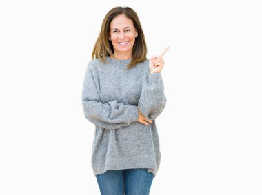 Yüzünde kocaman bir gülümseme ile izole arka plan üzerinde kış kazak giyen güzel orta yaş kadın kameraya bakarak yan el ve parmak ile işaret.