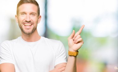Yakışıklı adam, yüzünde kocaman bir gülümseme ile rahat beyaz t-shirt giyen kameraya bakarak yan el ve parmak ile işaret.
