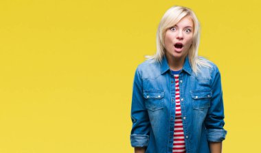 Korkuyor ve şok sürpriz ifade, korku ve heyecan yüz ile izole arka plan üzerinde kot ceket giyen genç güzel sarışın kadın.