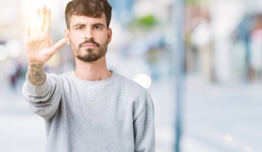 Elin avuç durağı şarkı yapıyor izole arka plan üzerinde sweatshirt giyen genç yakışıklı adam. Negatif ve ciddi bir jest yüz ifadesiyle uyarı.