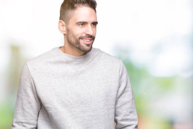 Uzak tarafına yüzünde, doğal ifade gülümseme ile seyir izole arka plan üzerinde sweatshirt giyen genç yakışıklı adam. Kendine güvenen gülüyor.