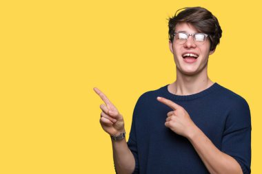 Gülümseyen ve iki elleri ve parmakları ile tarafına işaret kamera bakarak izole arka plan üzerinde gözlük takan genç yakışıklı adam.
