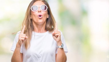 Moda güneş gözlüğü izole arka plan üzerinde giyen orta yaş İspanyol kadın hayrete ve yukarıya bakıp parmakları ile işaret şaşırttı ve silah kaldırdı.