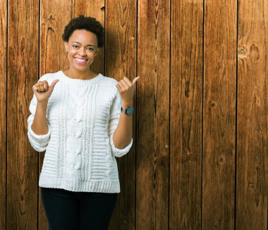 Üzerinde kazak giyen güzel genç Afro-Amerikan kadın izole arka plan emin gülümseyen arkasından el ve kadar başparmak ile işaret