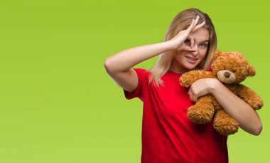 Sevimli Ayıcık ile mutlu yüz el parmaklarının arasından seyir göz üzerinde ok işaretiyle yapıyor gülümseyen izole arka plan üzerinde tutan genç beyaz kadın