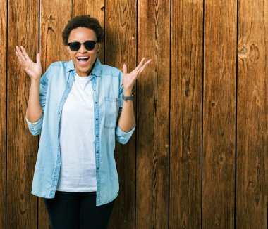 Arka plan deli kutluyor güzel genç Afro-Amerikan kadın üzerinde güneş gözlüğü takıyor izole ve crazy arms ile başarı için kaldırdı ve heyecanlı çığlık gözler kapalı. Kazanan kavramı