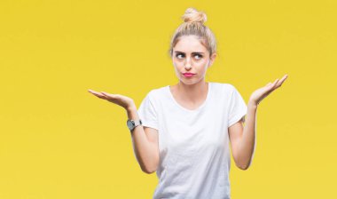 İzole arka plan clueless ve şaşkın bir ifadeyle kollar ve eller kaldırdı üzerinde beyaz t-shirt giyen genç güzel sarışın kadın. Şüphe kavramı.