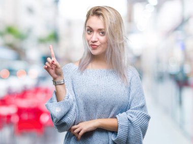 Kameraya bakarak yan el ve parmak ile işaret yüzünde kocaman bir gülümseme ile izole arka plan üzerinde kış kazak giyen genç sarışın kadın.