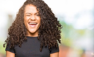 Genç güzel kadın kıvırcık saçlı seksi bir ifadeyle, neşeli ve mutlu yüzünü kameraya bakarak göz kırpıyor.