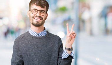 Genç yakışıklı mutlu yüz zafer işareti yaparken kameraya göz kırpıyor ile gülümseyen izole arka plan üzerinde gözlük takan adam akıllı. İki numaralı.