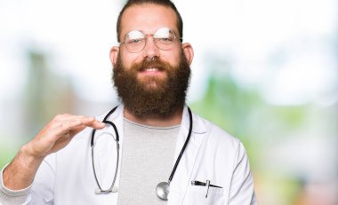 Sakal tıbbi giyen ile genç sarışın doktor erkek ceket ile büyük ve büyük boy işaret, ölçü birimi sembol gösteren el el hareketi. Kameraya bakarak gülümsüyordu. Ölçüm kavramı.