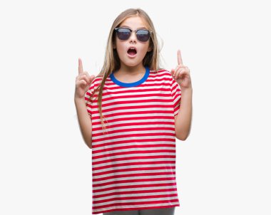 Genç güzel kız hayran ve yukarıya bakıyor ve parmakları ile işaret ve silah kaldırdı sürpriz izole arka plan üzerinde güneş gözlüğü takıyor.