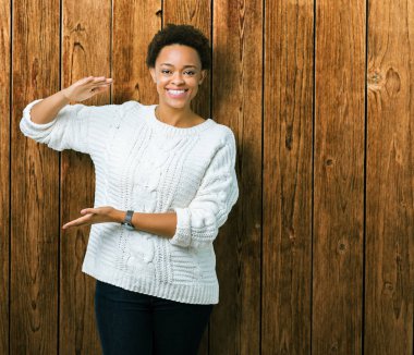 Büyük ve büyük boy işaret, ölçü birimi sembol gösteren ellerle eller izole arka plan üzerinde kazak giyen güzel genç Afro-Amerikan kadın. Kameraya bakarak gülümsüyordu. Ölçüm kavramı.