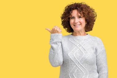 Seyir ve başparmak yanında yukarıyı mutlu yüz ile gülümseyen izole arka plan üzerinde kış kazak giyen güzel orta ager üst düzey kadın.