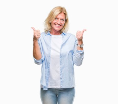 Orta yaş sarışın kadın el ile pozitif jest yapıyor izole arka plan başarı işareti yüzünden başparmak gülümseyen ve mutlu. Neşeli bir ifadeyle, kazanan jest kameraya bakıyor.