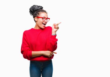 Genç saç Afro-Amerikan Kız giyiyor kazak ve gözlük yüzünde kocaman bir gülümseme ile izole arka plan üzerinde kameraya bakarak yan el ve parmak ile işaret örgülü.