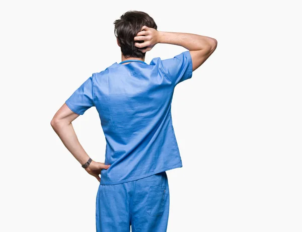 年轻的医生穿着医疗制服在孤立的背景向后思考怀疑与手在头 — 图库照片
