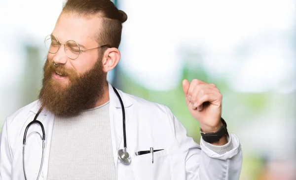 Young blond doctor man with beard wearing medical coat Dancing happy and cheerful, smiling moving casual and confident listening to music