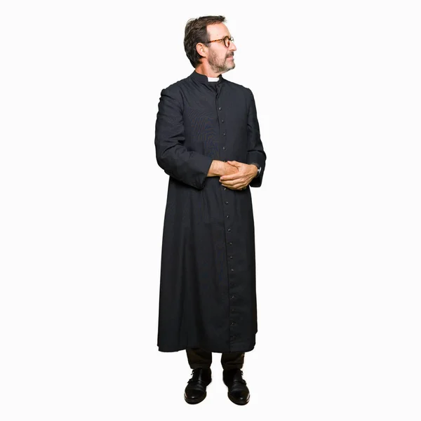 中年牧师男子穿着天主教长袍微笑着看着一边双臂交叉的信心和信心 — 图库照片