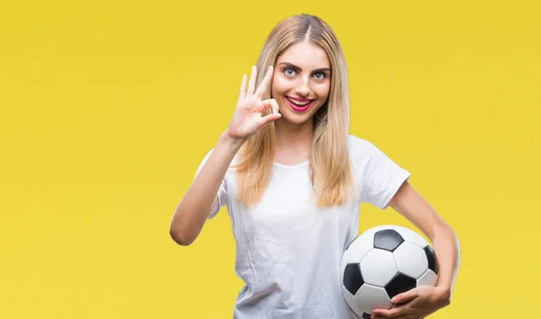 年轻美丽的金发碧眼的女人拿着足球在孤立的背景做确定的标志与手指 优秀的象征 — 图库照片