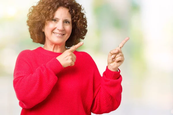 美丽的中间年龄的老年妇女红色冬天毛衣在孤立的背景微笑 看着相机指向用两只手和手指的一侧 — 图库照片
