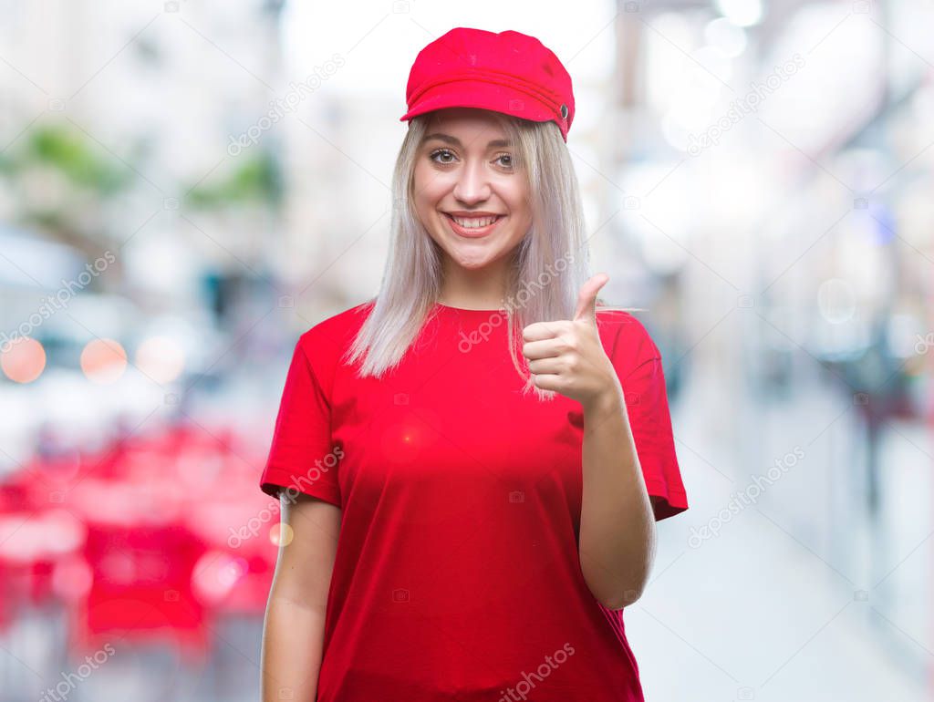 Young blonde woman wearing red hat over isolated background doing happy thumbs up gesture with hand. Approving expression looking at the camera with showing success.