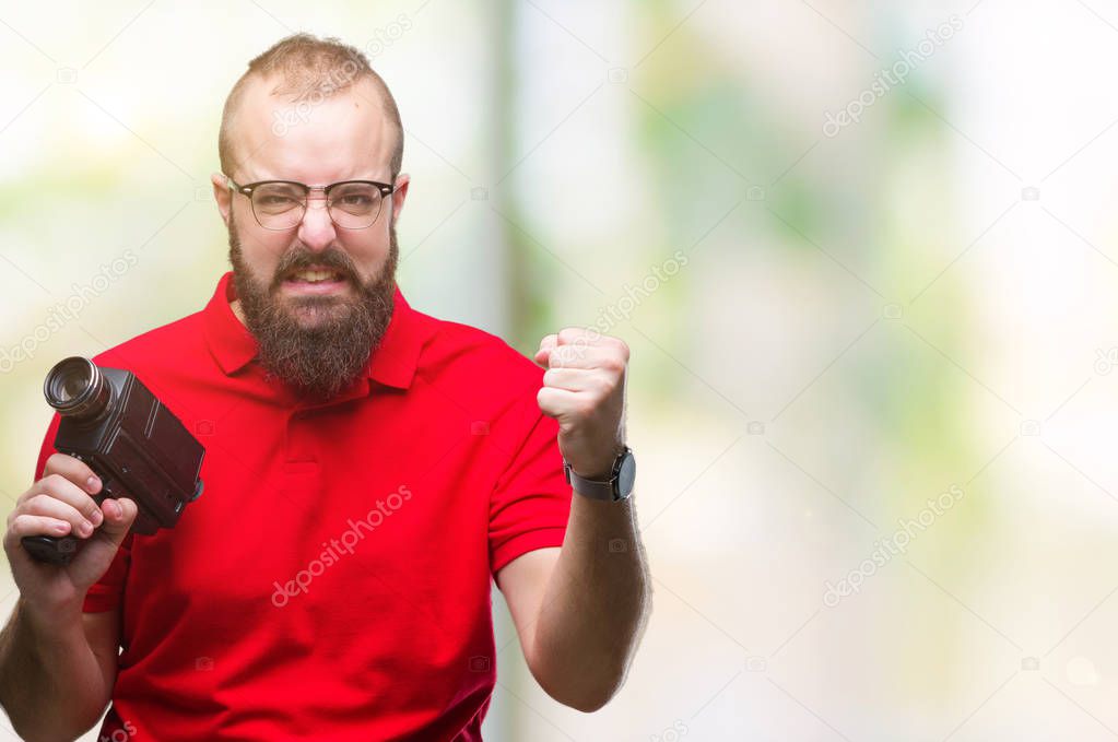 Young caucasian hipster man filmming using retro video camera over isolated background annoyed and frustrated shouting with anger, crazy and yelling with raised hand, anger concept