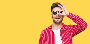 Genç yakışıklı adam giyen güneş gözlüğü el gülümseyen, ok jest yapıyor göz parmakları ile mutlu yüz üzerinden seyir.