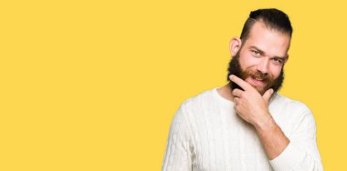 Emin çapraz kollar ve çeneme kaldırdı el ile gülümseme ile kameraya bakarak kış kazak giyen genç hipster adam. Pozitif düşünce.