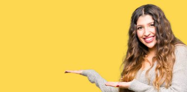 Genç güzel kadın giyiyor kış işaretçi el yanında giysi ve açık palm, mutlu ve kendine güvenen reklam gülümseyen sunulması