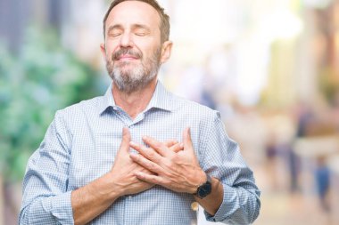 Orta yaş ağarmış üst düzey iş adamı izole arka plan ile gülümseyen üzerinde kapalı gözler ve yüzünde minnettar jest ile göğüs üzerinde eller. Sağlık kavramı.