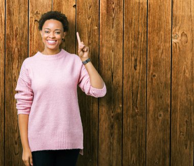 Güzel, genç, Afro-Amerikalı bir kadın izole edilmiş arka planda bir numarayı gösterip işaret ederken kendine güvenen ve mutlu bir şekilde gülümsüyor..