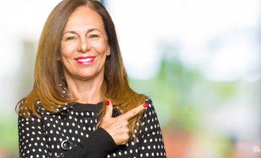 Neşeli bir gülümseme ile el ve parmak kadar yan yüzünde mutlu ve doğal ifade ile işaret yüz ile moda ceket giyen güzel orta yaş kadın