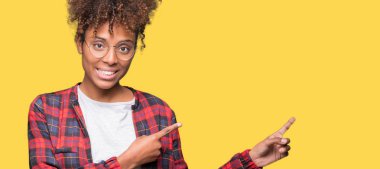 Güzel genç Afro-Amerikan kadın gülümseyerek ve iki elleri ve parmakları ile tarafına işaret kamera bakarak izole arka plan üzerinde gözlük.