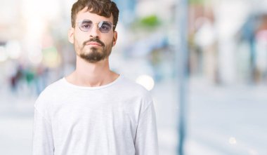 Genç yakışıklı adam yüzünde ciddi bir ifade ile izole arka plan üzerinde güneş gözlüğü takıyor. Basit ve doğal kameraya bakıyor.