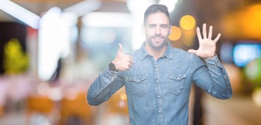 Yakışıklı delikanlı gösterilen ve parmakları ile işaret izole arka plan üzerinde kendinden emin ve mutlu gülümseyerek süre 6 numara.