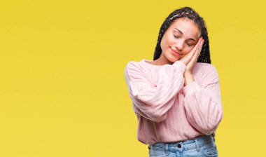 Genç uyku yorgun hayal ve ellerle birlikte poz ile kapalı gözler gülümseyen izole arka plan üzerinde kazak giyen Afro-Amerikan kız saç örgülü.