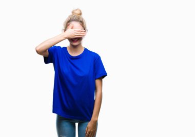 Genç güzel sarışın ve mavi gözlü kadın gülümsüyor ve gözleri için sürpriz kapsayan yüz el ile gülüyor izole arka plan üzerinde mavi tişört giyiyor. Kör kavramı.