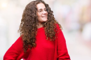 Güzel esmer kıvırcık saçlı Genç kız üzerinde gözlük ve kış kazak giyiyor arka plan uzak tarafına gülümseme ile yüzünde, doğal ifade arıyorum izole. Kendine güvenen gülüyor.