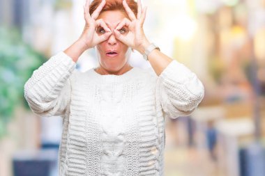 Dilini, parmaklarının arasından baktığını yapışmasını dürbün gibi ok jest yapıyor izole arka plan üzerinde kış kazak giyen Atrractive üst düzey beyaz Kızıl saçlı kadın. Deli ifade.