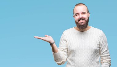 Neşeli sunulması ve kameraya bakarak avucunun ile işaret gülümseyen izole arka plan üzerinde kış kazak giyen genç beyaz hipster adam.