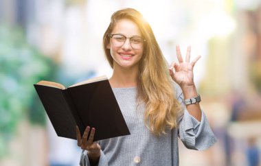 Genç güzel sarışın kadın parmakları, mükemmel sembolü olan ok işareti yapıyor izole arka plan üzerine bir kitap okuma