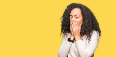 Kıvırcık saçlı rahat kazak giyen genç güzel kız el ağzıyla kapsayan yorgun esneme sıkılmış. Restless ve uyku hali.