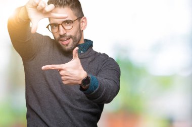 Elle yapma çerçeve ve parmakları ile mutlu yüz gülümseyen izole arka plan üzerinde gözlük takan yakışıklı delikanlı. Yaratıcılık ve Fotoğrafçılık kavramı.