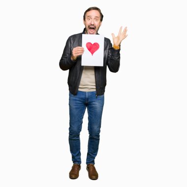 Kocaman bir gülümseme ile çığlık ve ellerini kaldırdı zaferini kutluyor kırmızı kalp çok mutlu ve heyecanlı, kazanan ifade ile kağıt tutan yakışıklı orta yaş erkek