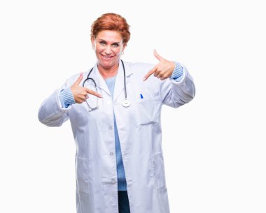 Yüzünde gülümseme ile kendinden emin görünüyorsun, kendini gururlu ve mutlu parmakları ile işaret izole arka plan üzerinde tıbbi üniforma giyen üst düzey beyaz doktor kadın.